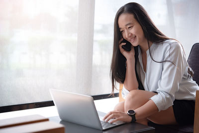 Young woman using phone while sitting on table