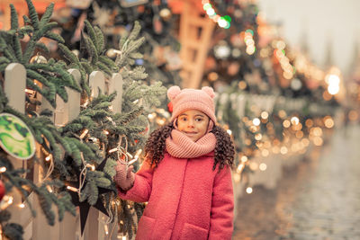 Portrait of smiling young woman standing by christmas tree