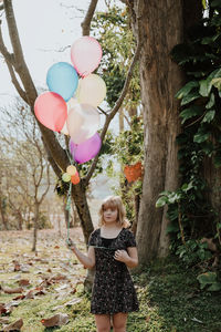 Young woman holding balloons while standing on field