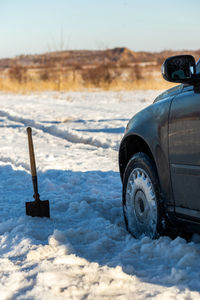 A vehicle stuck in the snow in wild field at daylight with shovel sticking out from snow near