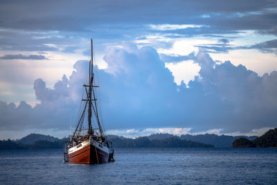 Boat sailing on sea against cloudy sky