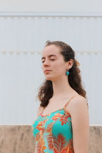 Young woman looking away while standing against wall