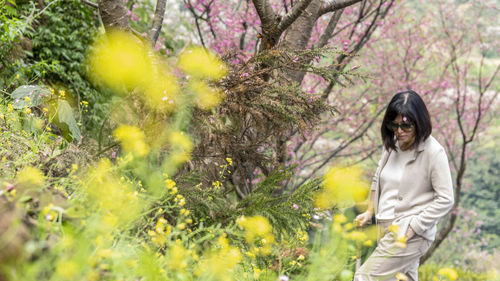 Full length of young woman standing against yellow flowering plants