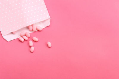 Directly above shot of gumballs from paper bag on pink background