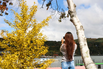 Rear view of woman standing by tree against sky