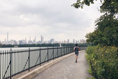 Rear view of man jogging on promenade in city