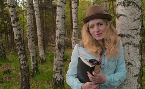 Portrait of young woman with book by tree in forest