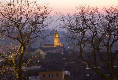 Bare trees and buildings against sky at dusk