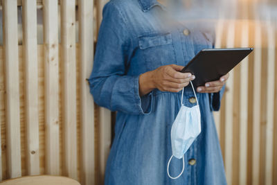 Midsection of female entrepreneur holding digital tablet and protective face mask standing in cafe