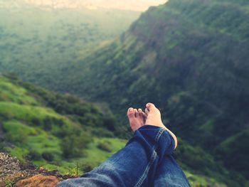 Low section of man relaxing against green mountains
