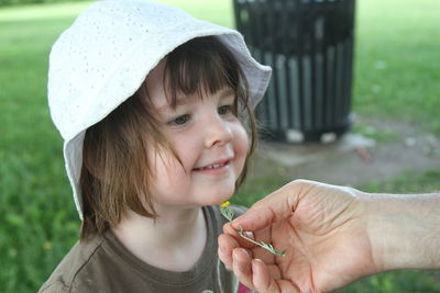 Cropped hand of mother ticking cute daughter with flower on face in park