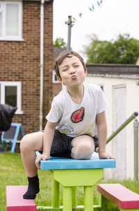 Cute boy puckering while sitting on table at backyard