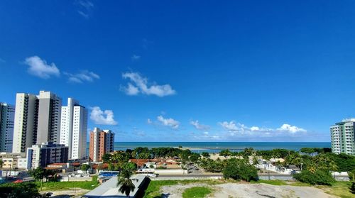 City buildings by sea against blue sky