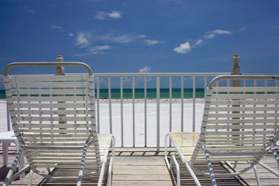 Chairs on railing by sea against sky