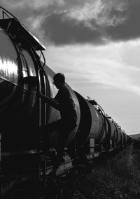 Man standing on ladder of train against sky