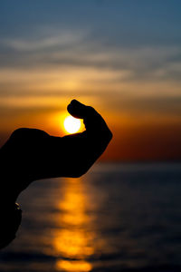 Silhouette hand against orange sunset sky