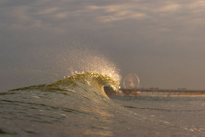 Sea waves splashing on shore against sky during sunrise