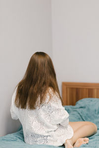 Rear view of woman sitting on bed at home