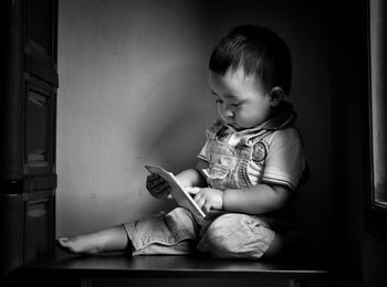 Cute baby boy holding book while sitting on floor at home