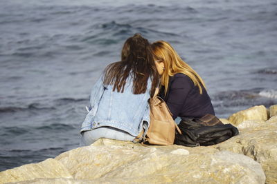 Rear view of woman sitting on rock at beach
