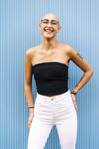 Happy young woman with eyeglasses standing in front of blue wall