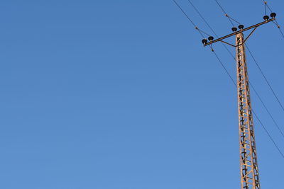 Low angle view of electricity pylon against clear blue sky