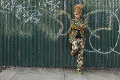 Portrait of girl standing on sidewalk against wall