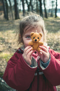 Portrait of girl holding teddy bear while standing on field