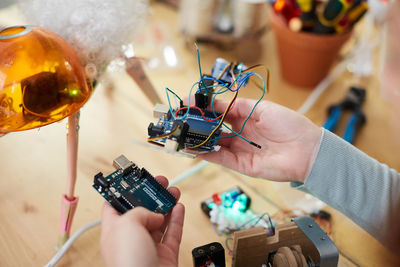 Cropped hands of young female technician holding electrical equipment at table in workshop