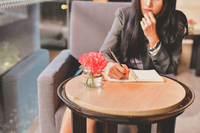 Midsection of woman holding coffee while sitting on table in restaurant