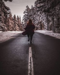 Rear view of woman walking on road amidst trees during winter