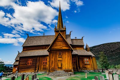 View on the cemetery, medieval stave church in lom, mountains against cloudy sky on a sunny day