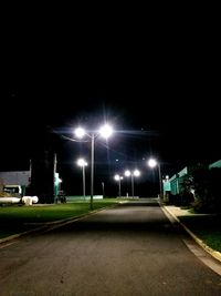 Illuminated street lights on road in city against sky at night