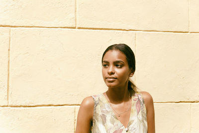 Young woman looking away while standing by wall outdoors