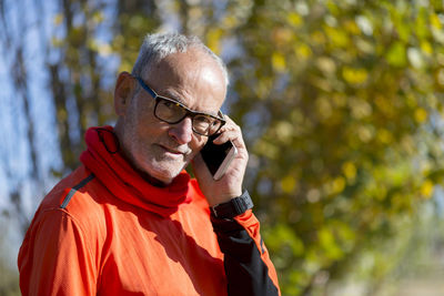 Portrait of senior man talking on mobile phone against trees