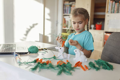 Cute girl doing craft while watching videos on laptop at home