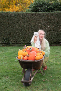 Middle-aged blonde woman at a large cart with ripe pumpkins and a small kitten