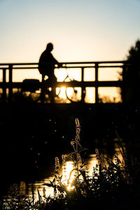 Silhouette man standing on bridge over lake against sky during sunset