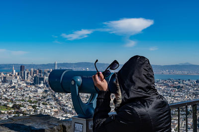 Man photographing with cityscape in background against blue sky