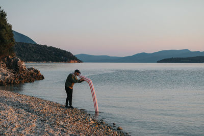 Man standing on rock by sea against sky