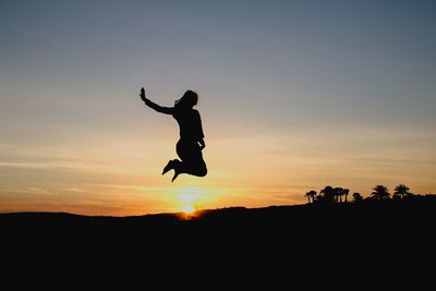 Silhouette man jumping against sky during sunset