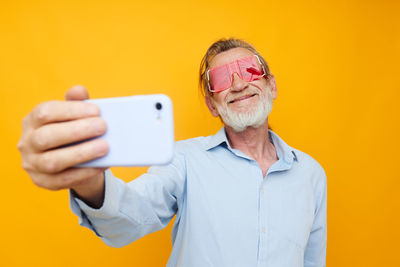 Young man using mobile phone against yellow background