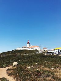 Lighthouse on field by building against clear blue sky