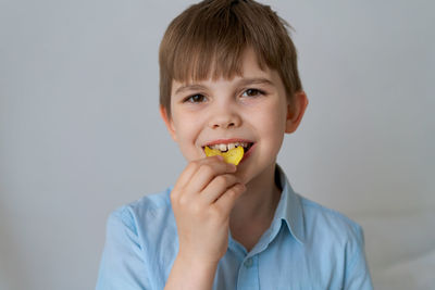 Young little caucasian child eating unhealthy potato chips on a gray background