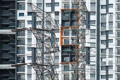 Low angle view of electricity pylons against building in city