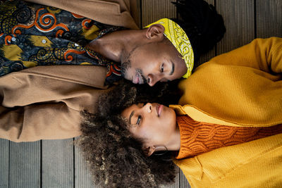 Top view of trendy african american man and woman in bright coat lying opposite with face to face looking at each other