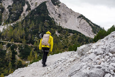 Rear view of hiker wearing hiking clothes and gear, walking on rocky path in mountains