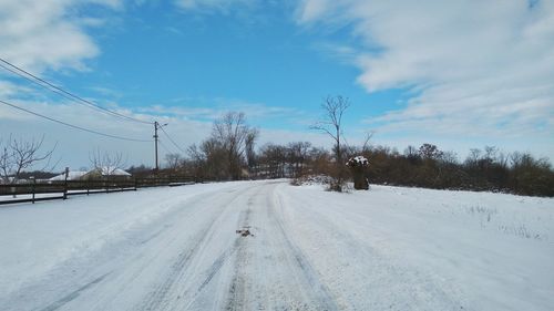 Road by trees against sky during winter