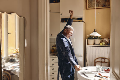 Side view of mature man dancing with hand raised in kitchen at home