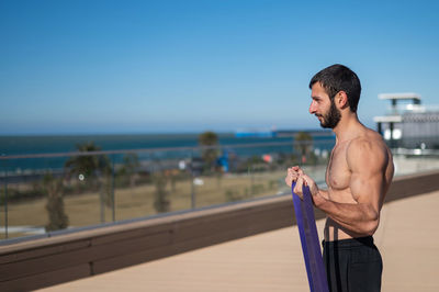 Shirtless man doing exercise with rubber bands outdoors. 